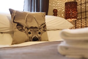 Una cama con un cojín de diseño de ciervo, una lámpara y un papel tapiz estampado al fondo.