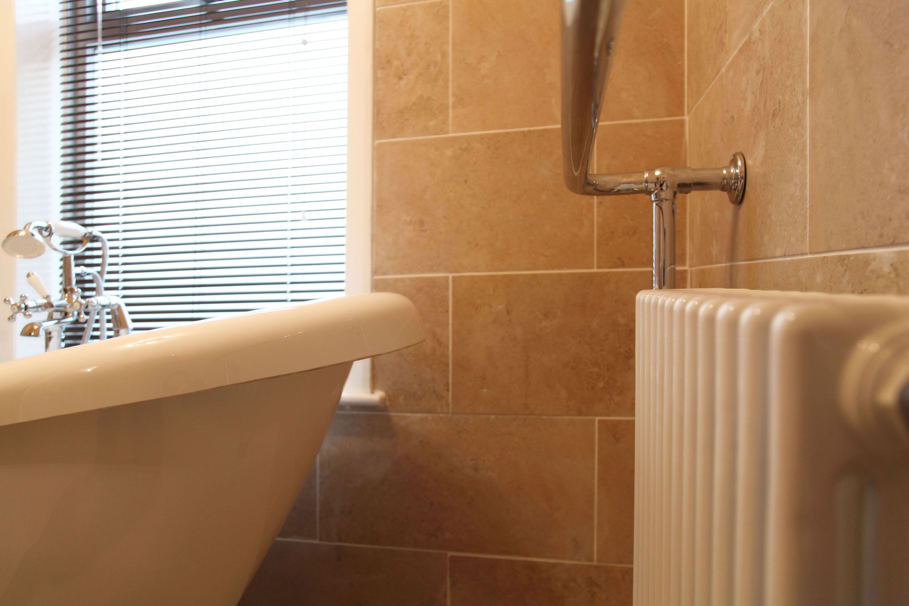 A bathroom with a bathtub, a radiator, and a window with blinds.