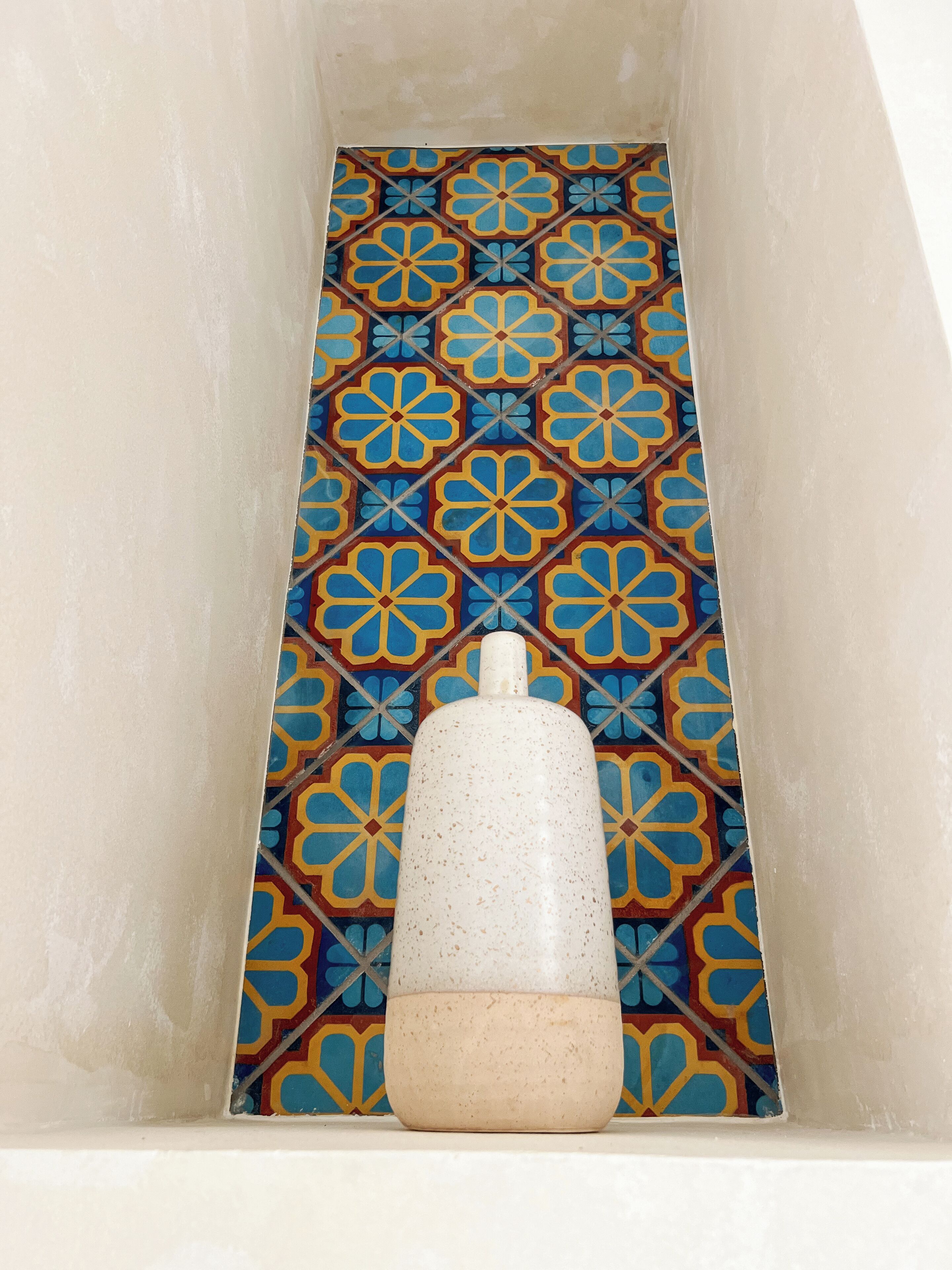 Una bañera con un diseño geométrico de azulejos y un objeto blanco en el centro.
