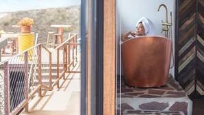 A person relaxing in a large copper bathtub on a balcony with a view of the hills. - Native Residence (Playas de Rosarito)