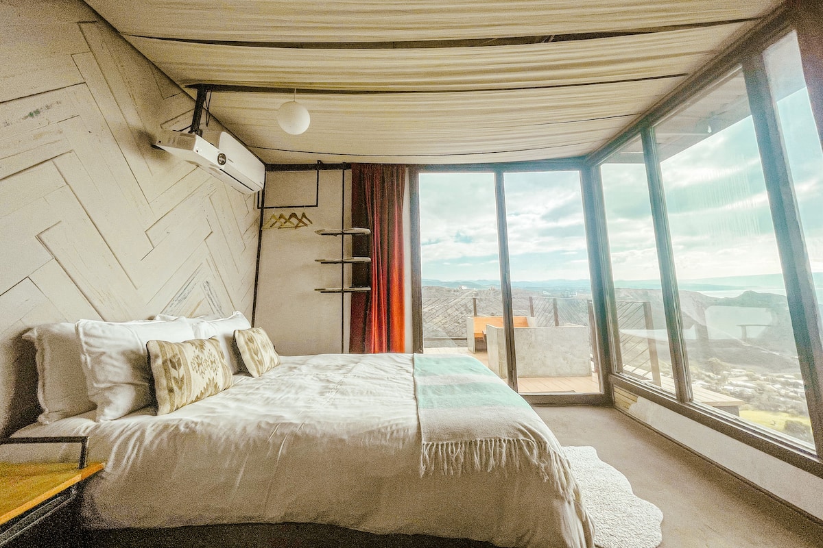 A bedroom with a large bed, a view of the city, and a unique ceiling design.