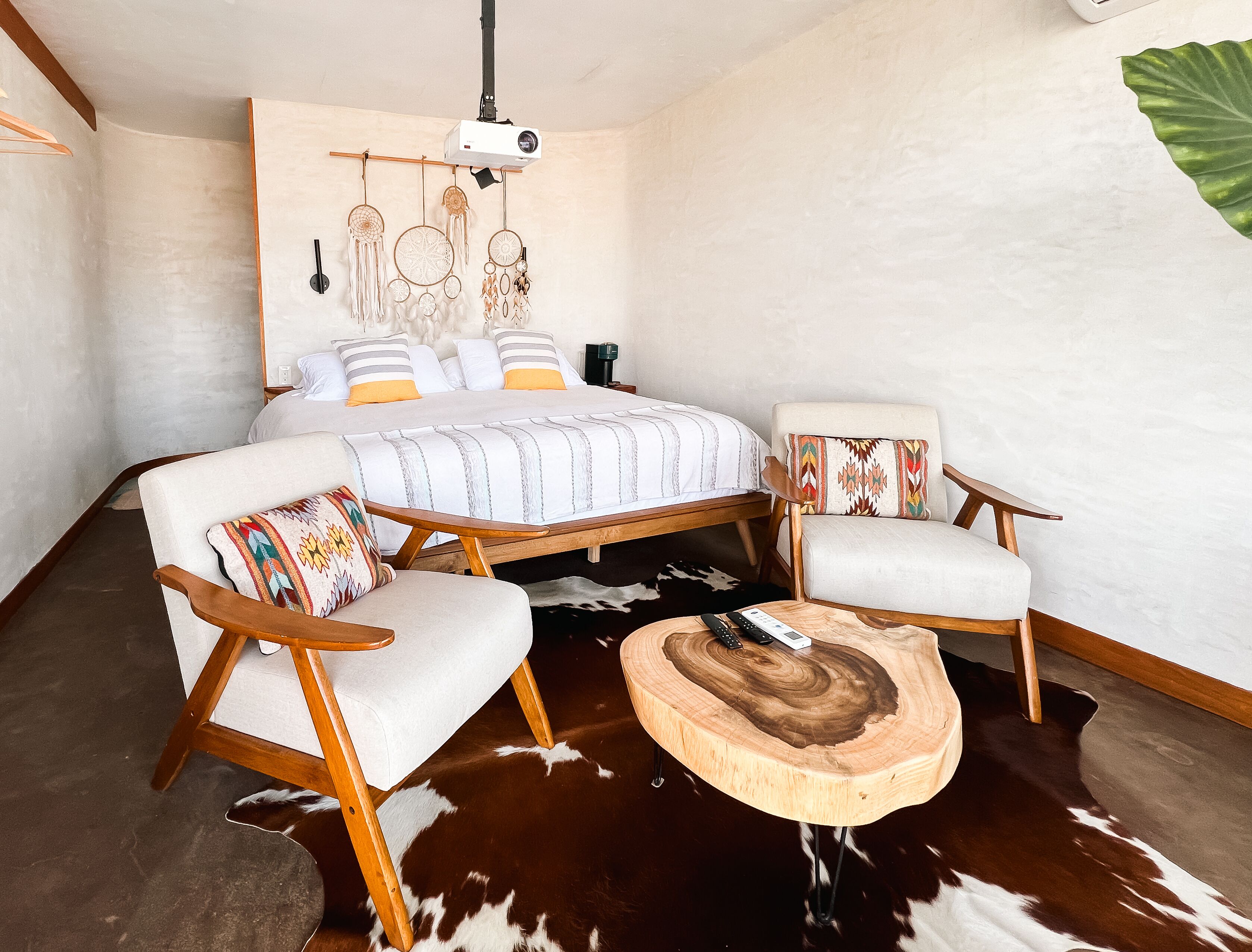 A bedroom with a large bed, two wooden chairs, a round wooden coffee table, and a cowhide rug.