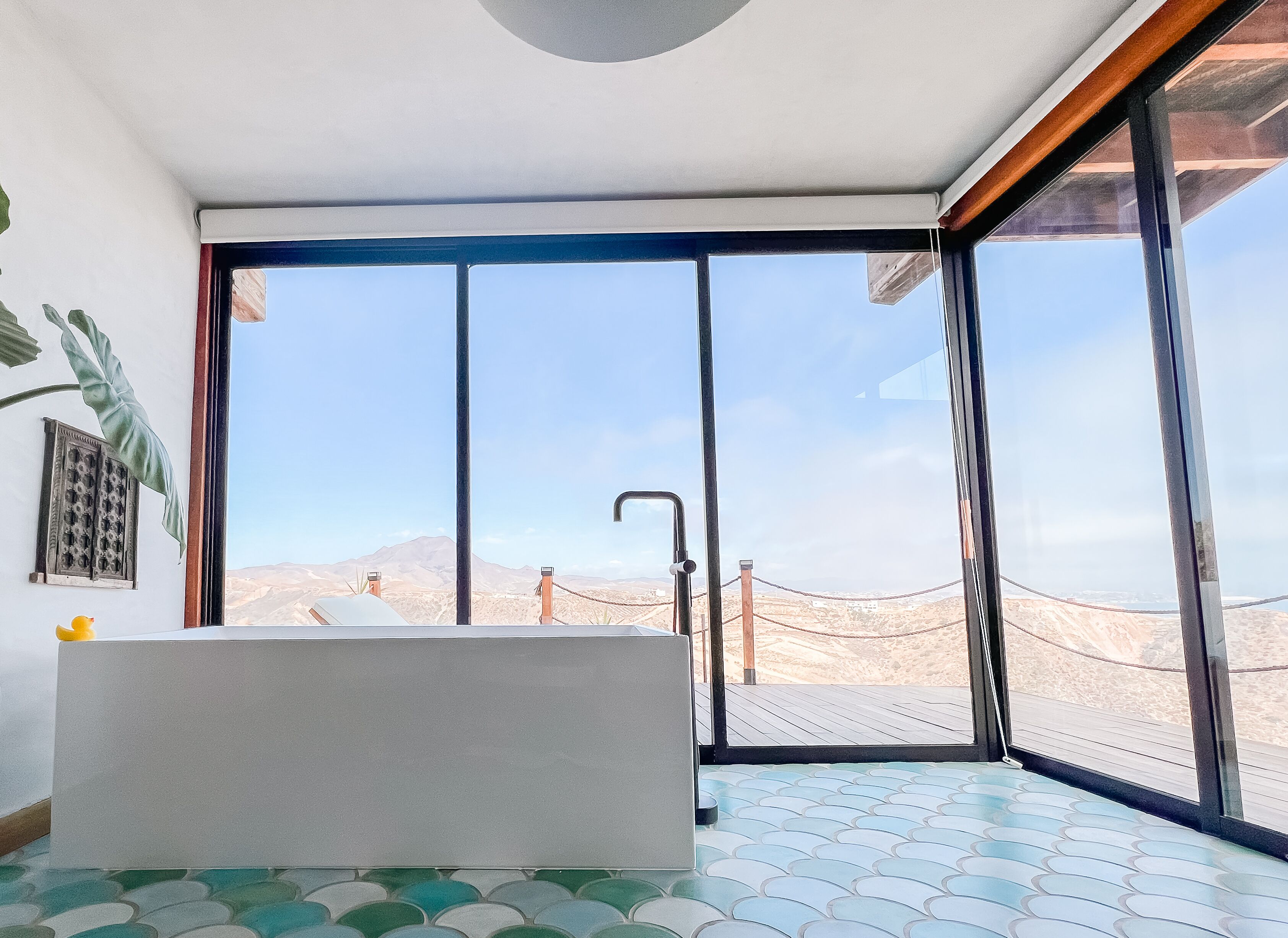 A modern bathroom with a large bathtub, a window with a view of a desert landscape, and a patterned floor.