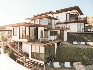 Una casa moderna de varios pisos con balcón, mobiliario exterior y una escalera.