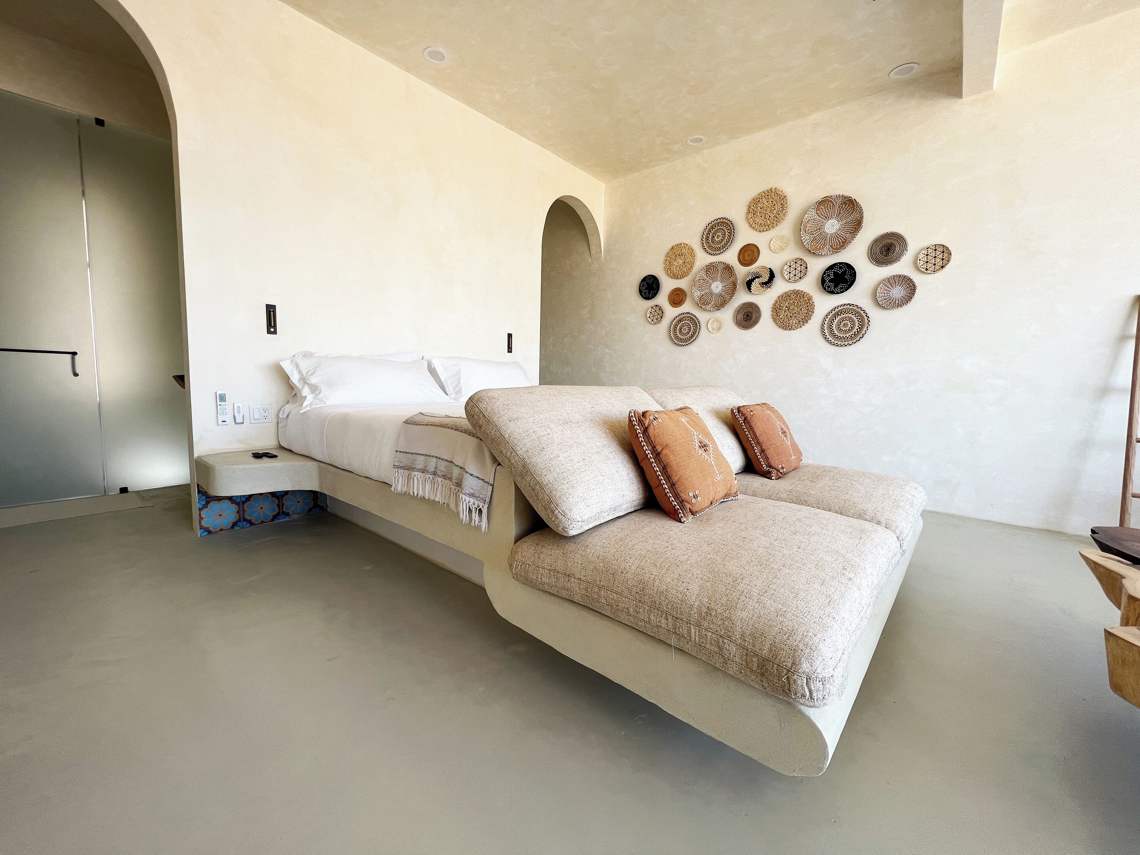 A modern bedroom with a sofa bed, a bedside table, and a wall decorated with woven baskets.
