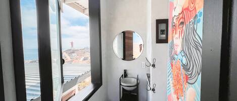 A bathroom with a large window, a sink, a mirror, and a colorful mural.