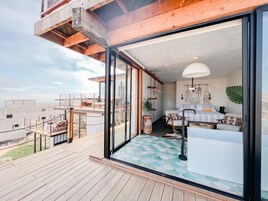 A modern interior with a large glass door leading to a balcony. The room features a white sofa, a coffee table, and a hanging light fixture.