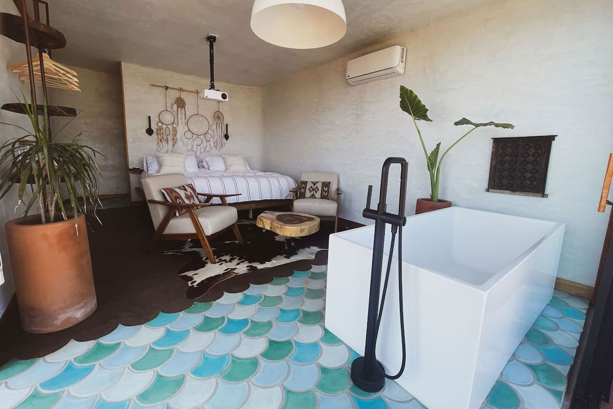 A bedroom with a bed, a white bathtub, a ceiling projector, and a wall-mounted air conditioner.