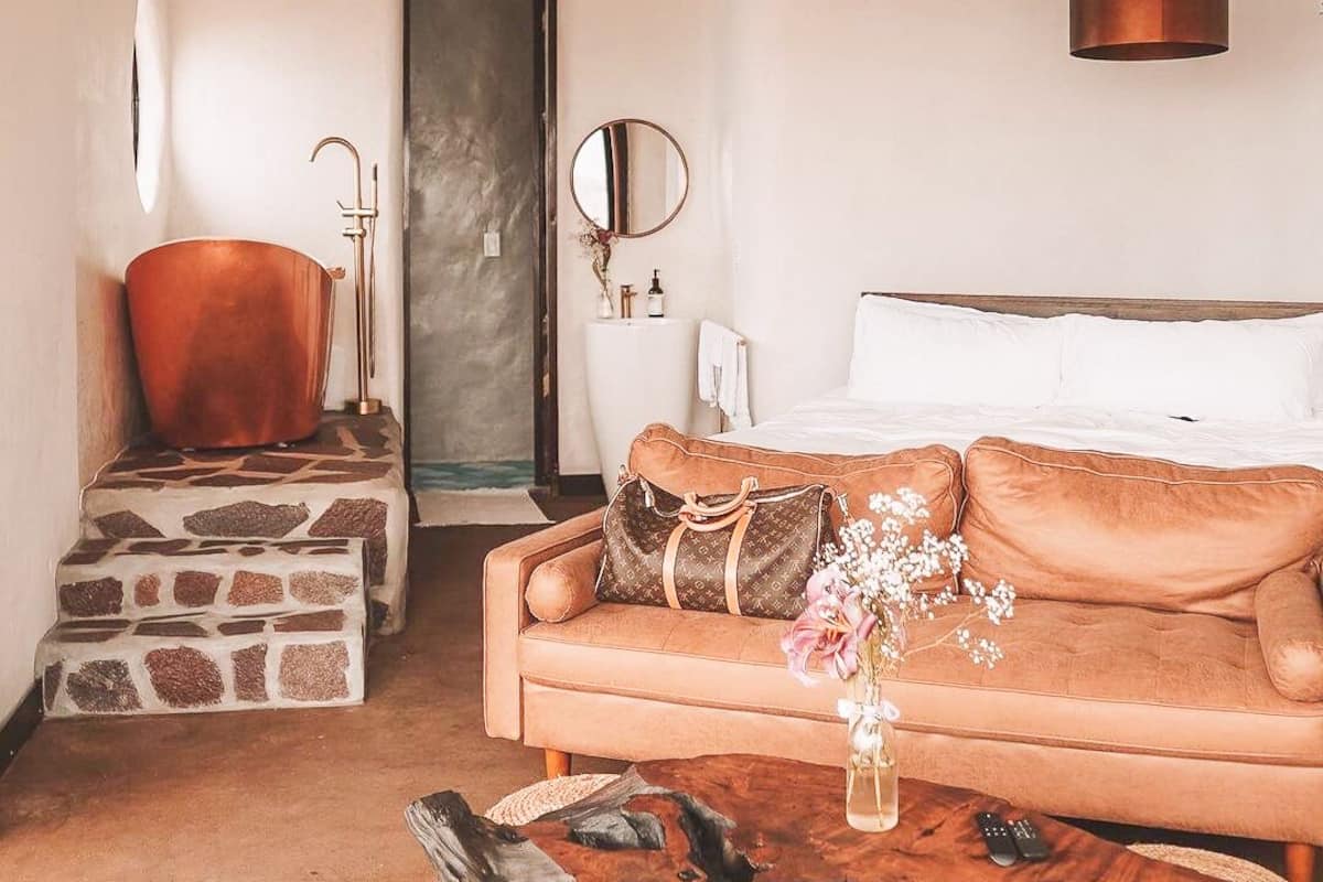 A cozy bedroom with a stone staircase, a copper bathtub, a wooden coffee table, and a brown sofa with a decorative vase.