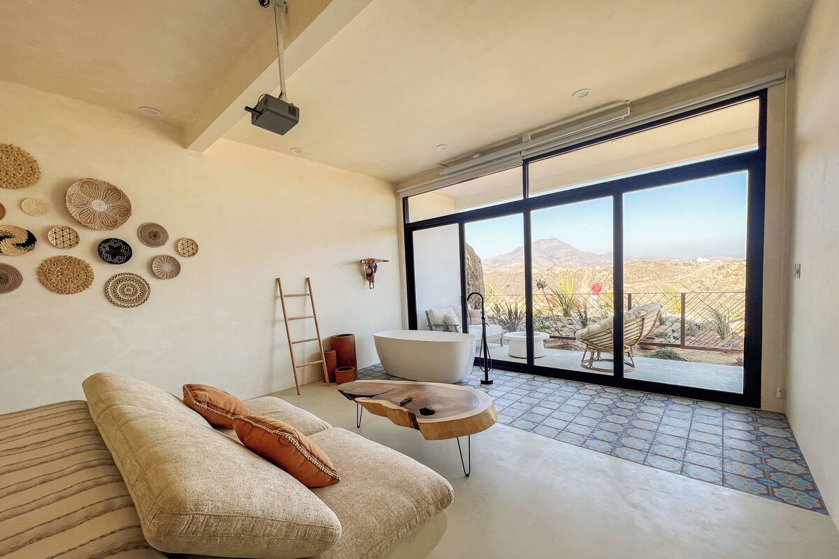 A modern living room with a large window, a bathtub, and a variety of decorative items on the wall.