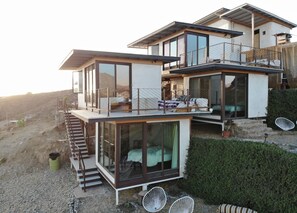 A modern two-story house with large glass windows, a balcony, and a staircase leading to the upper floor.