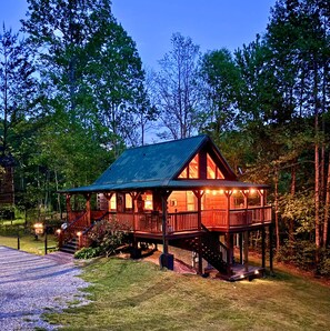 A wooden cabin with a porch and a deck, surrounded by trees.