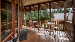 A wooden porch with a table and chairs, large windows, and a view of trees. - Maietok Lis i Gory (Polyanitsya)