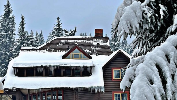 A two-story wooden cabin with a snow-covered roof and icicles hanging from the eaves. - Maietok Lis i Gory (Polyanitsya)