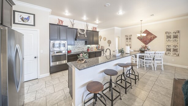 A modern kitchen with dark cabinets, a granite island, and bar stools. - Enormous house with new backyard (Midland)