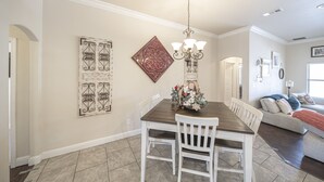 A dining area with a wooden table and white chairs, a decorative chandelier, and wall art. - Enormous house with new backyard (Midland)