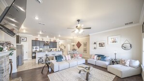A spacious living room with a fireplace, a kitchen in the background, and a ceiling fan. - Enormous house with new backyard (Midland)