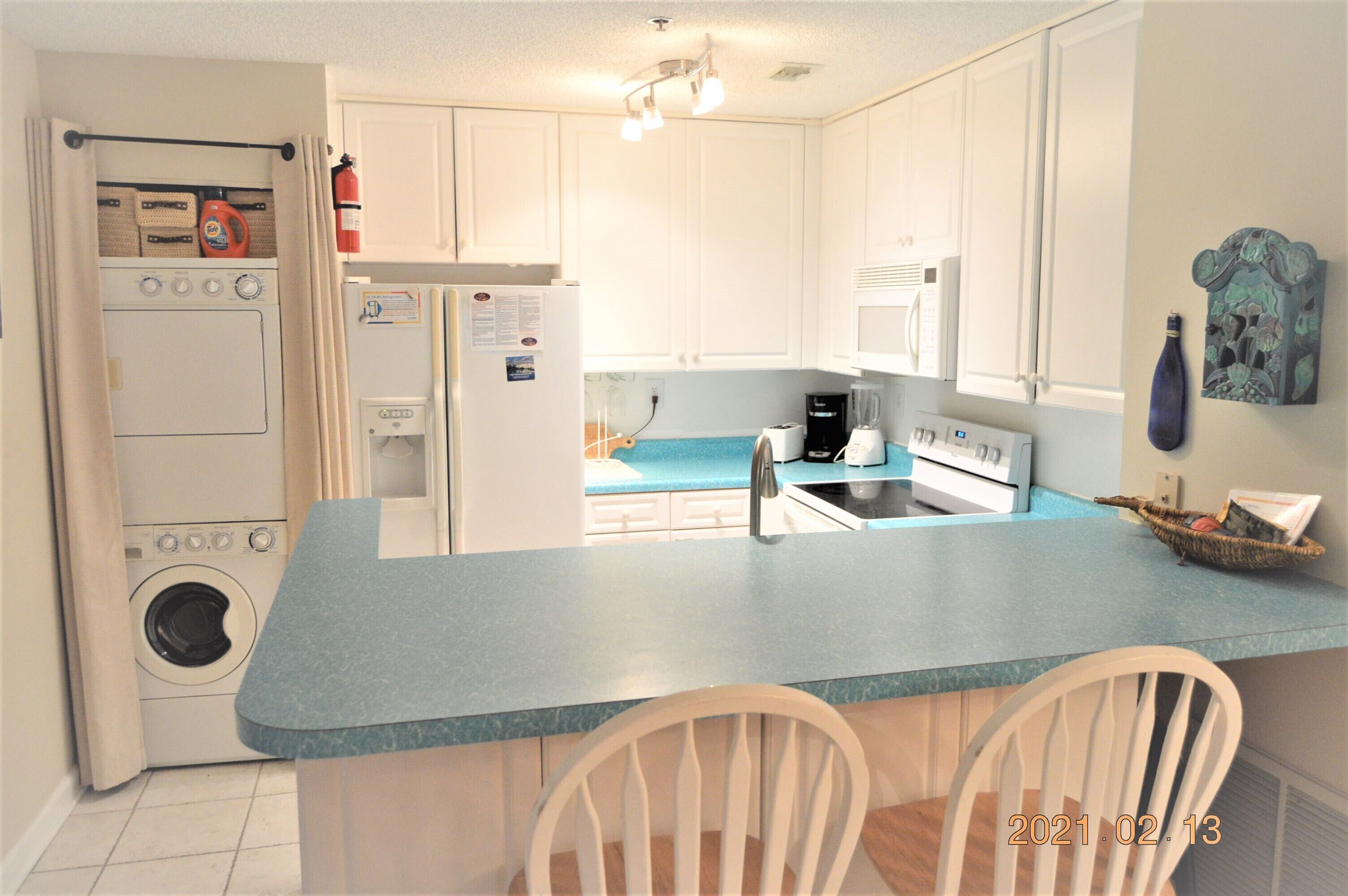 A compact kitchen with a washing machine, a refrigerator, a coffee maker, and a sink.