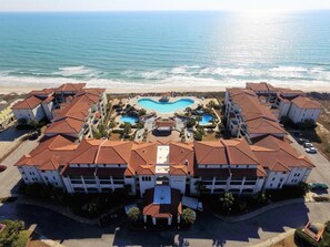 A resort with a central swimming pool, beachfront location, and multiple buildings with red-tiled roofs.