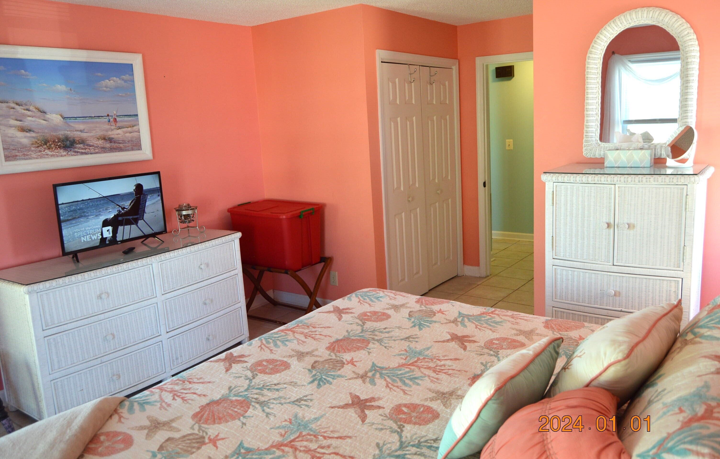 A bedroom with a bed, dresser, television, and a mirror.