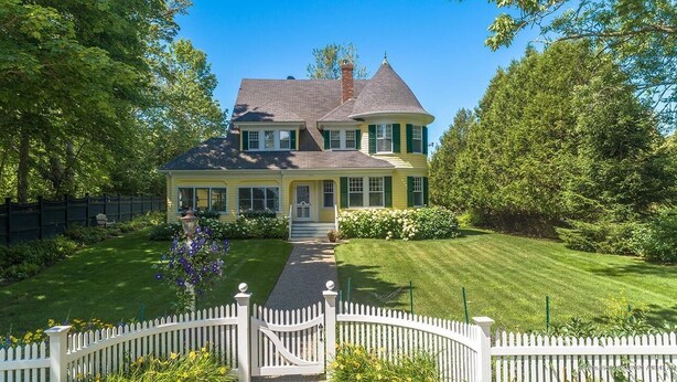 A two-story house with a wrap-around porch, a front yard with a white picket fence, and a well-maintained lawn. - MASSIVE Oceanfront Dark Harbor Home on ISLESBORO (Islesboro)