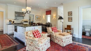 A spacious kitchen with white cabinetry, a central island, and a dining area with two floral-patterned chairs. - MASSIVE Oceanfront Dark Harbor Home on ISLESBORO (Islesboro)