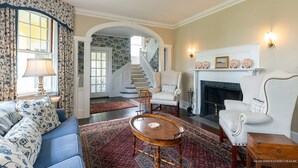 A traditional living room with a sofa, armchairs, a fireplace, and a staircase. - MASSIVE Oceanfront Dark Harbor Home on ISLESBORO (Islesboro)