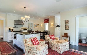 A spacious kitchen with white cabinetry, a central island, and a dining area with two floral-patterned chairs.