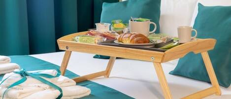 A neatly made bed with teal bedding, a wooden tray with breakfast items, and a pair of folded towels.