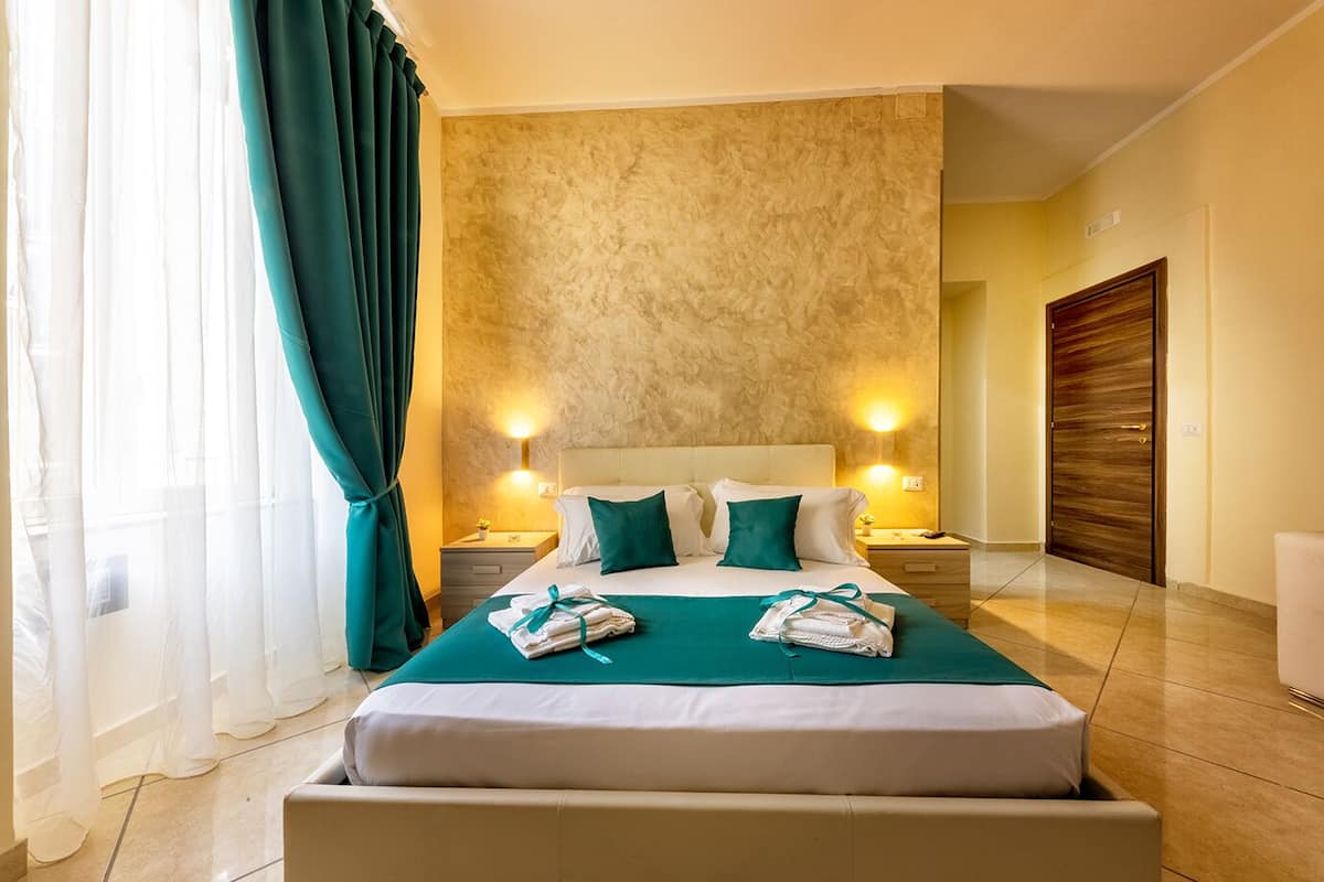 A hotel room with a large bed, two bedside tables, a wooden door, and a view of the outside.