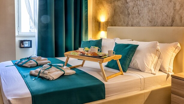 A hotel room with a bed, a bedside table with a tray of breakfast, a window with curtains, and a wall-mounted light. - Re Diego (Naples)