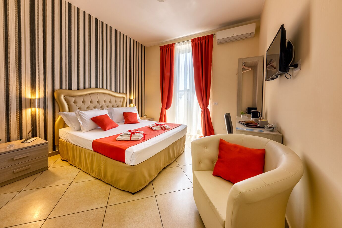 A hotel room with a large bed, a bedside table, a chair, a TV, and a window with curtains.