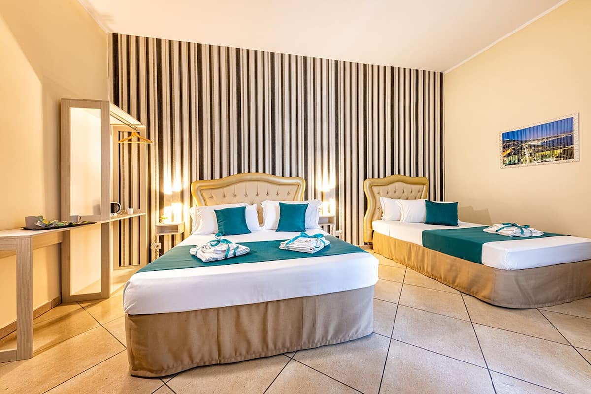A hotel room with two beds, a desk, a mirror, and a striped wall.