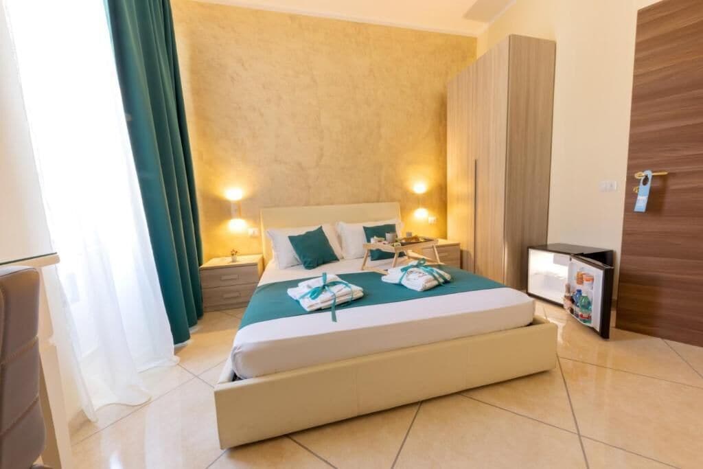 Quarto de hotel com uma cama grande, duas mesas de cabeceira, um guarda-roupa e um pequeno frigorífico.