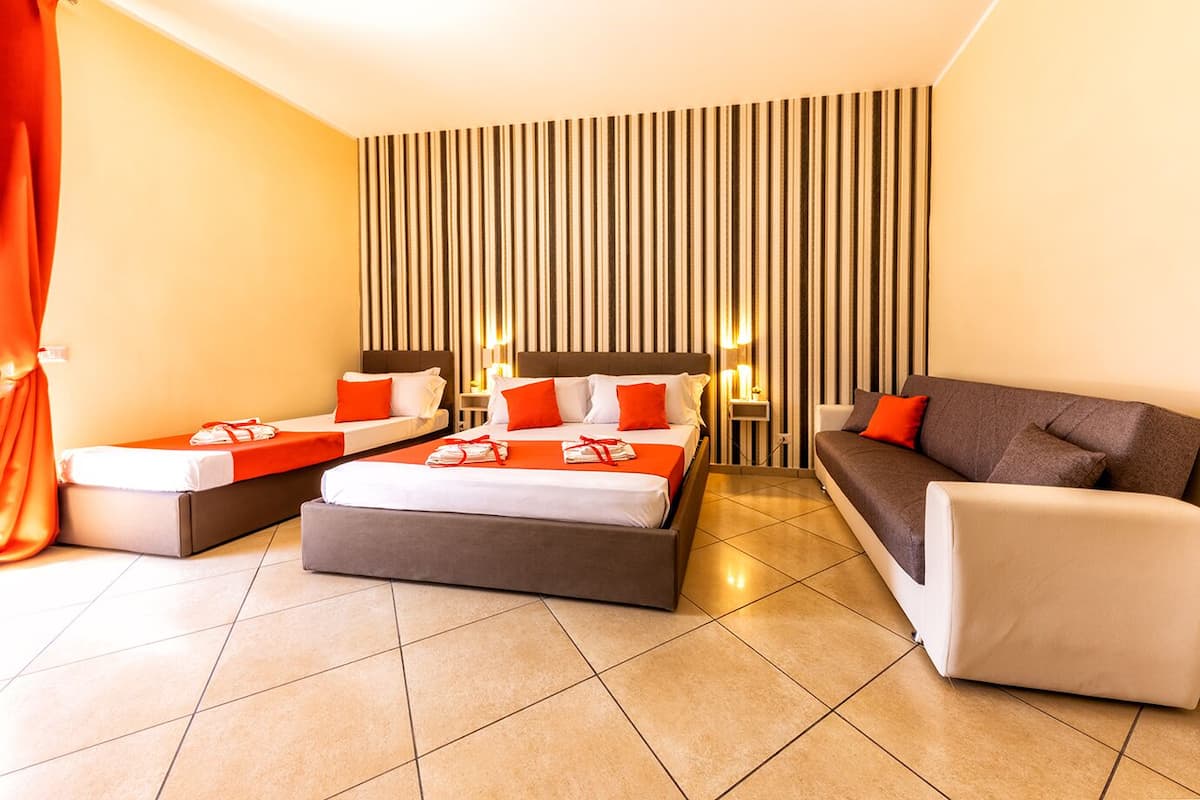 A hotel room with a large bed, a sofa, and a small table. There are striped walls and a tiled floor.