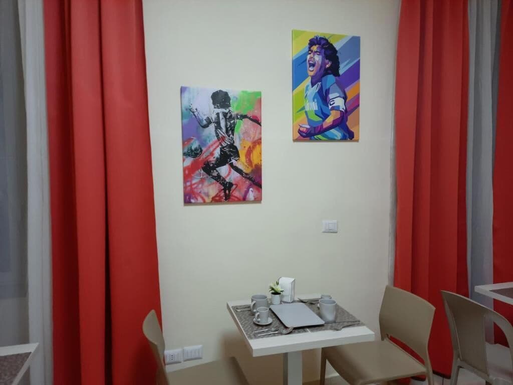 A room with a dining table set for two, a small plant on the table, and two paintings on the wall.