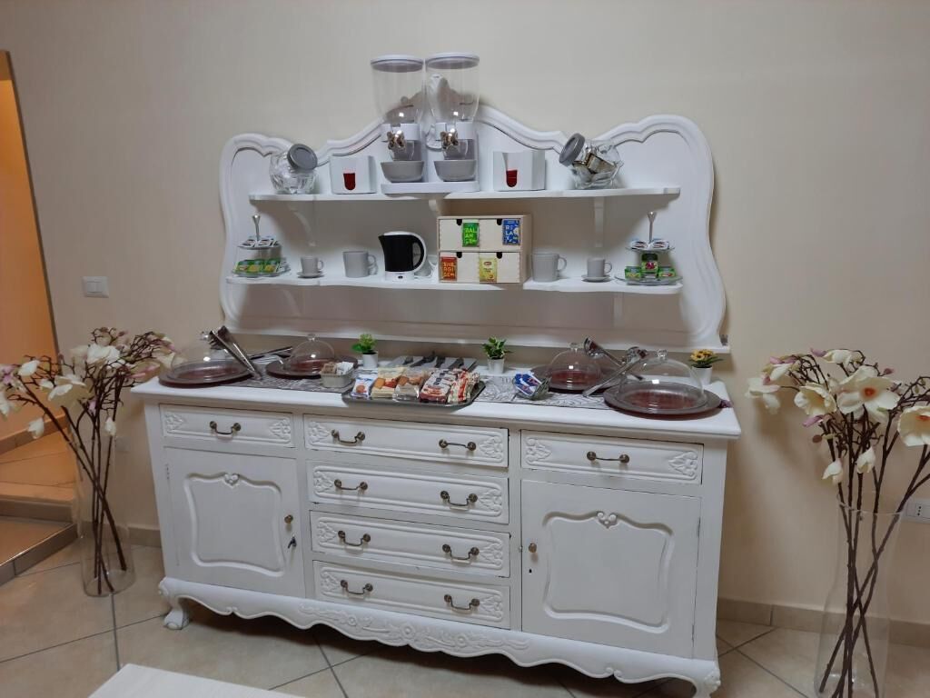 Una mesa de buffet blanca con varias estanterías, una máquina de café y diversos alimentos.