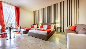A hotel room with a large bed, a sofa, a dining table, and a view of the city. - Re Diego (Naples)