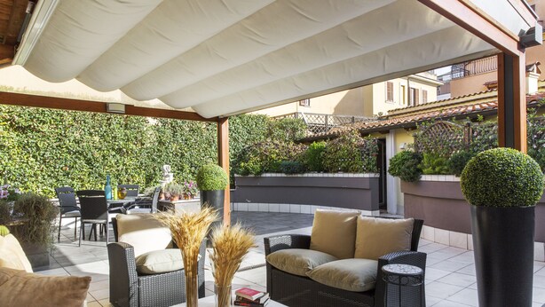 Un patio al aire libre con mobiliario de mimbre, una mesa blanca y plantas en macetas.