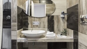Un baño moderno con un lavamanos ovalado grande, un espejo redondo y un perchero para toallas.