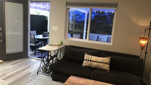 A modern living room with a dark sofa, a wooden coffee table, and a patterned rug. A dining table with chairs is visible in the background. - Artfully Curated Loft-Like Studio (Culver City)