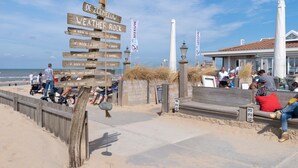 A beachside area with wooden signs indicating weather conditions, a sandy walkway, and people relaxing. - Salty Beach House near Beach and city centre (Noordwijk)