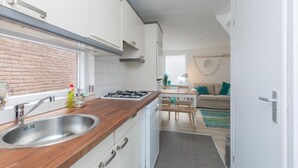 A modern kitchen with a brick backsplash, stainless steel sink, and wooden countertop. There is a dining area with a table and chairs, and a living room with a sofa and a window. - Salty Beach House near Beach and city centre (Noordwijk)