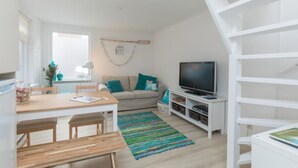 A modern living room with a sofa, TV, wooden dining table, and a staircase. - Salty Beach House near Beach and city centre (Noordwijk)