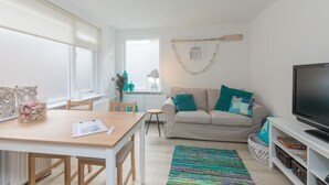 A modern living room with a sofa, a TV, a dining table, and a colorful rug. - Salty Beach House near Beach and city centre (Noordwijk)