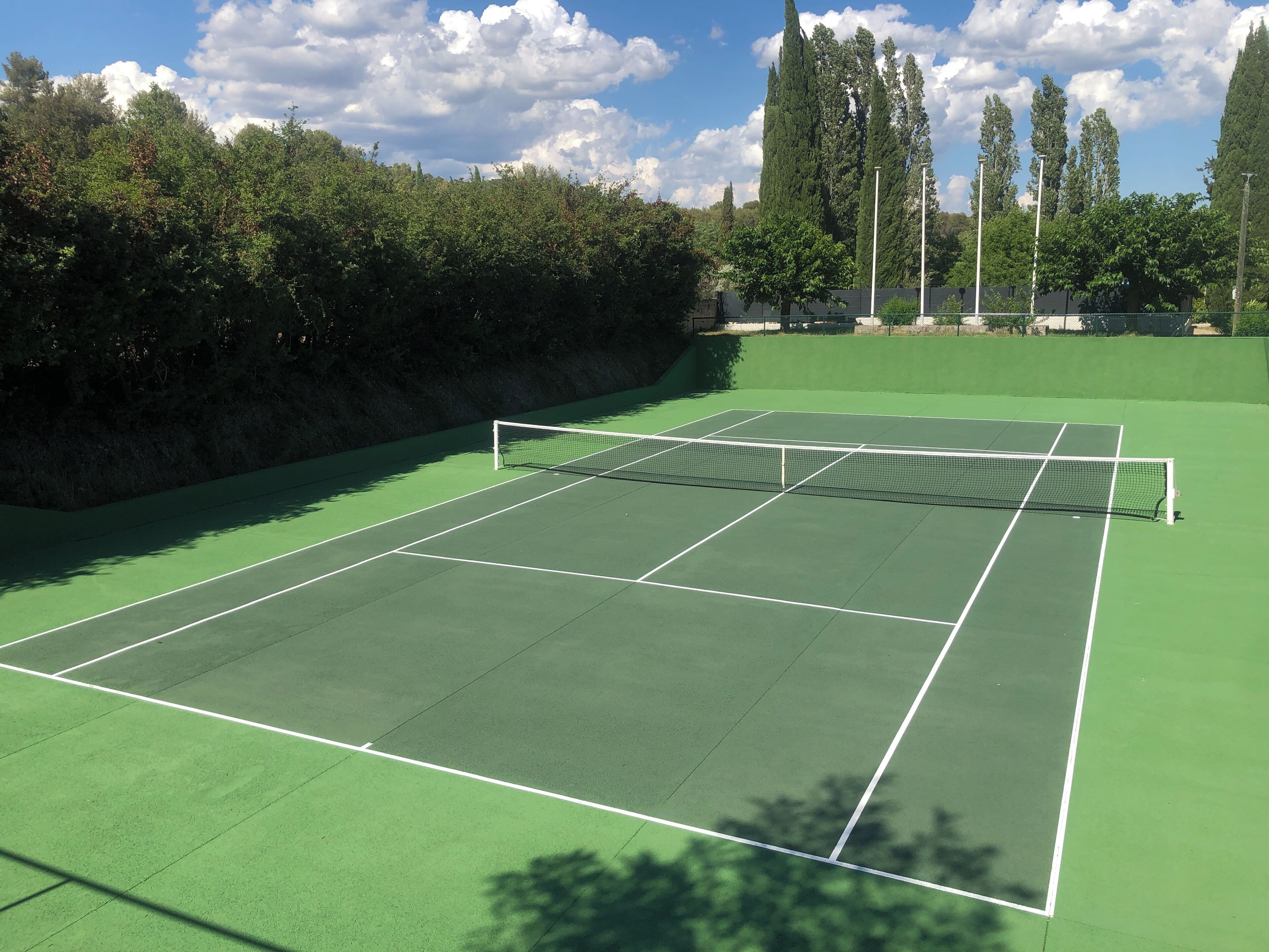 Un court de tennis avec un filet, entouré d’arbres et sous un ciel dégagé.
