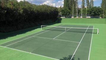 Un court de tennis avec un filet, entouré d’arbres et sous un ciel dégagé.