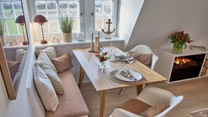 Un coin repas avec une table en bois mise pour deux personnes, un canapé et une cheminée.