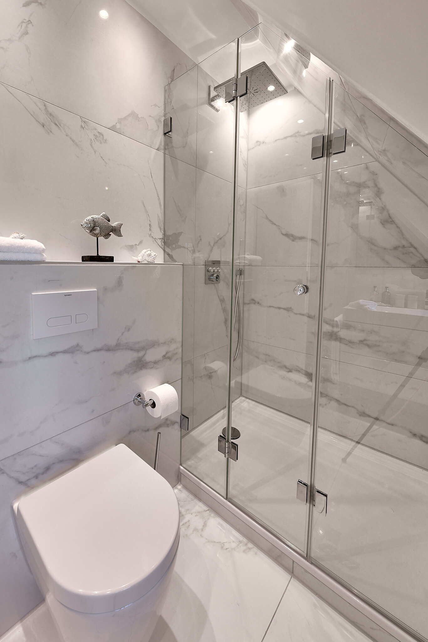 A modern bathroom with a glass-enclosed shower, a toilet, and marble walls.