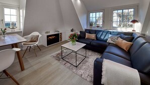 Un salon moderne avec un canapé bleu foncé, des fauteuils blancs, une table basse et une cheminée.